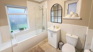 Un baño con bañera, inodoro, lavamanos y ventana con plantas.