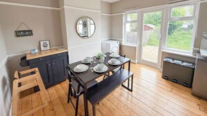 Una cocina con una mesa de comedor para cuatro, un banco de madera, una lámpara colgante y vistas al exterior a través de ventanas amplias.
