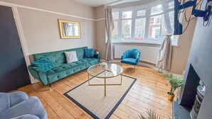 A modern living room with a green sofa, a blue armchair, and a glass coffee table.