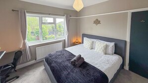 A bedroom with a bed, a desk, and a window with curtains.