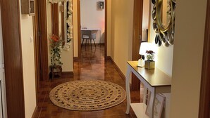 Un pasillo con piso de madera, un tapete redondo tejido, una consola blanca y un espejo montado en la pared.