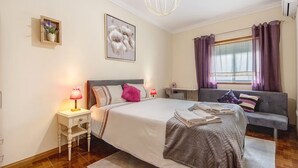 Un dormitorio con cama, mesita de noche, lámpara y ventana con cortinas.