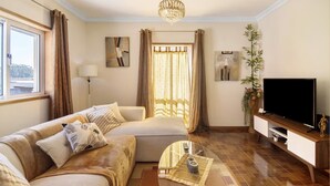 Una sala de estar bien iluminada con un sofá, una mesa de centro, un televisor y un ventanal con cortinas.