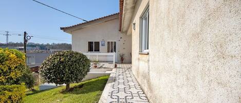 A building with a tiled walkway leading to a white door, surrounded by greenery and a clear sky.