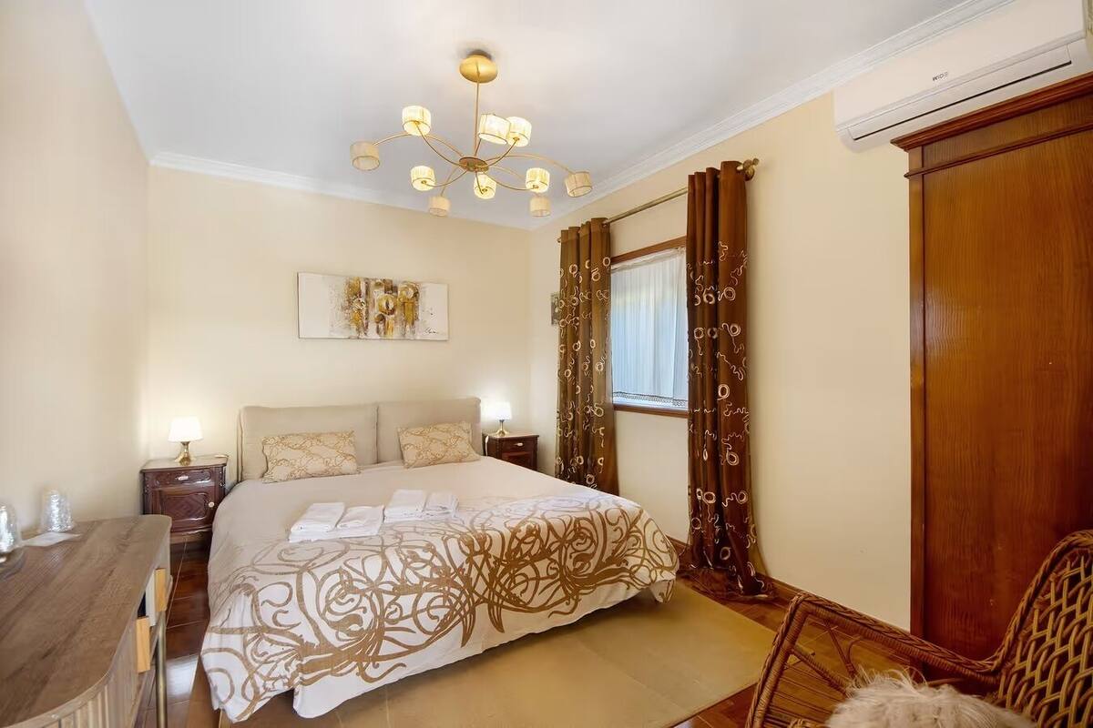 Un dormitorio con una cama grande, un candelabro, un armario de madera y una ventana con cortinas.