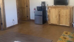 Ein Zimmer mit Holztür, Kühlschrank, Mikrowelle, Fernseher auf einer Holzkommode und einem gemusterten Teppich.