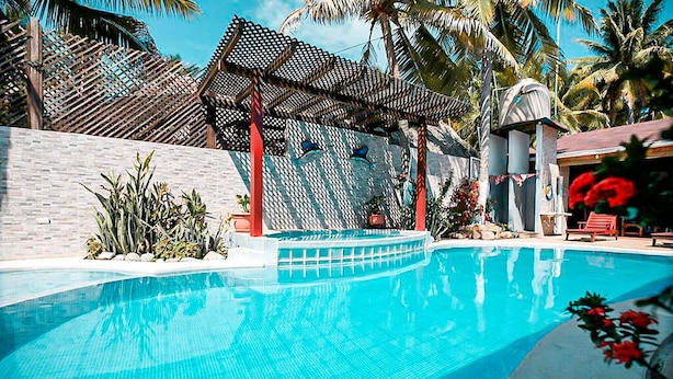 A swimming pool with a tiled edge, surrounded by palm trees and a wooden pergola. - Hotel Marlin Mi Paraiso (Taxisco)