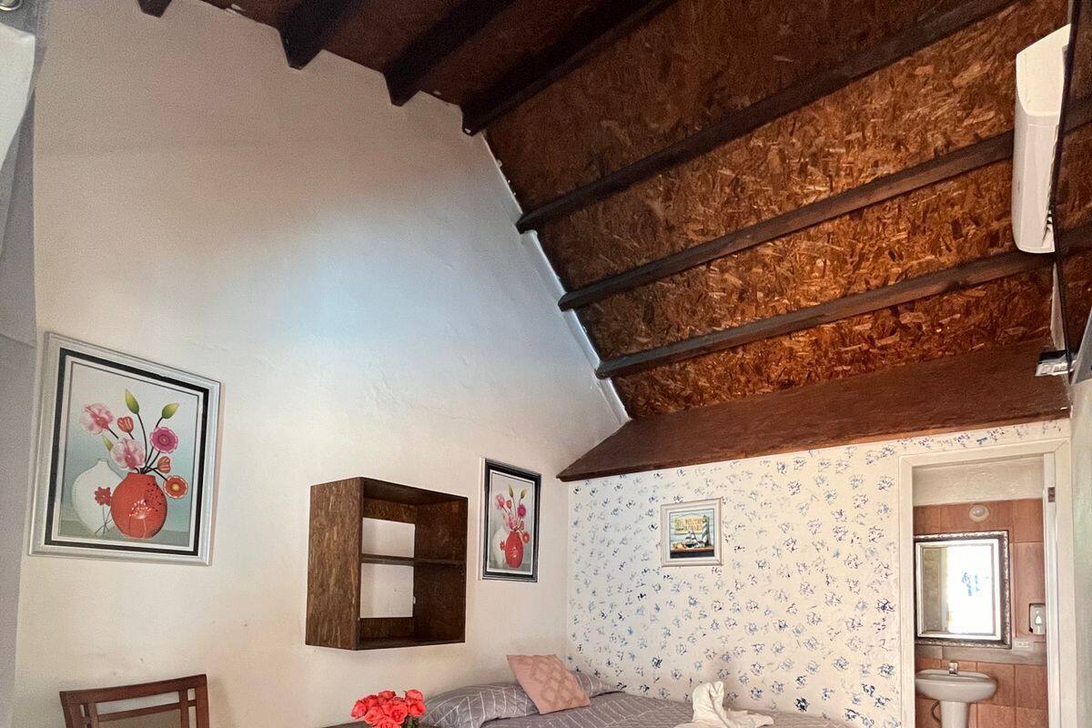 Ein gemütliches Schlafzimmer mit einem Bett, einem Holzstuhl, einem kleinen Tisch mit Blumen in einer Vase und einem Spiegel.