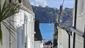 A narrow alleyway with white buildings, a red telephone booth, and a view of the sea with boats. - No 1 -  an apartment that sleeps 2 guests  in 1 bedroom (St Mawes)