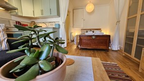 Un salon chaleureux avec un plancher en bois, une grande plante en pot, un canapé, une commode en bois et un lit avec des serviettes soigneusement pliées.