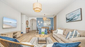 Een moderne woonkamer met een televisie, rieten stoelen, een bank en een eethoek met een blauwe wand en houten meubels.
