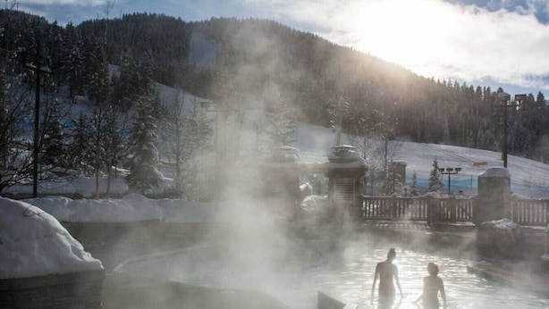A hot spring area with steam rising, surrounded by snow-covered trees and a mountain in the background. - Moguls | Lofted Ski in Ski Out w/ Hot Tub Access (Panorama)