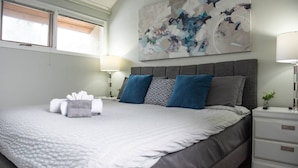 A neatly made bed with a white comforter and gray pillows, a bedside table with a lamp, and a large abstract painting on the wall. - Moguls | Lofted Ski in Ski Out w/ Hot Tub Access (Panorama)