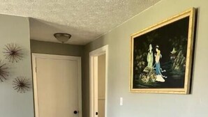 A hallway with two grey upholstered chairs, a wooden floor, a door, and a framed painting on the wall. - Historic Peaceful Apt near VSU & SGMC (Valdosta)