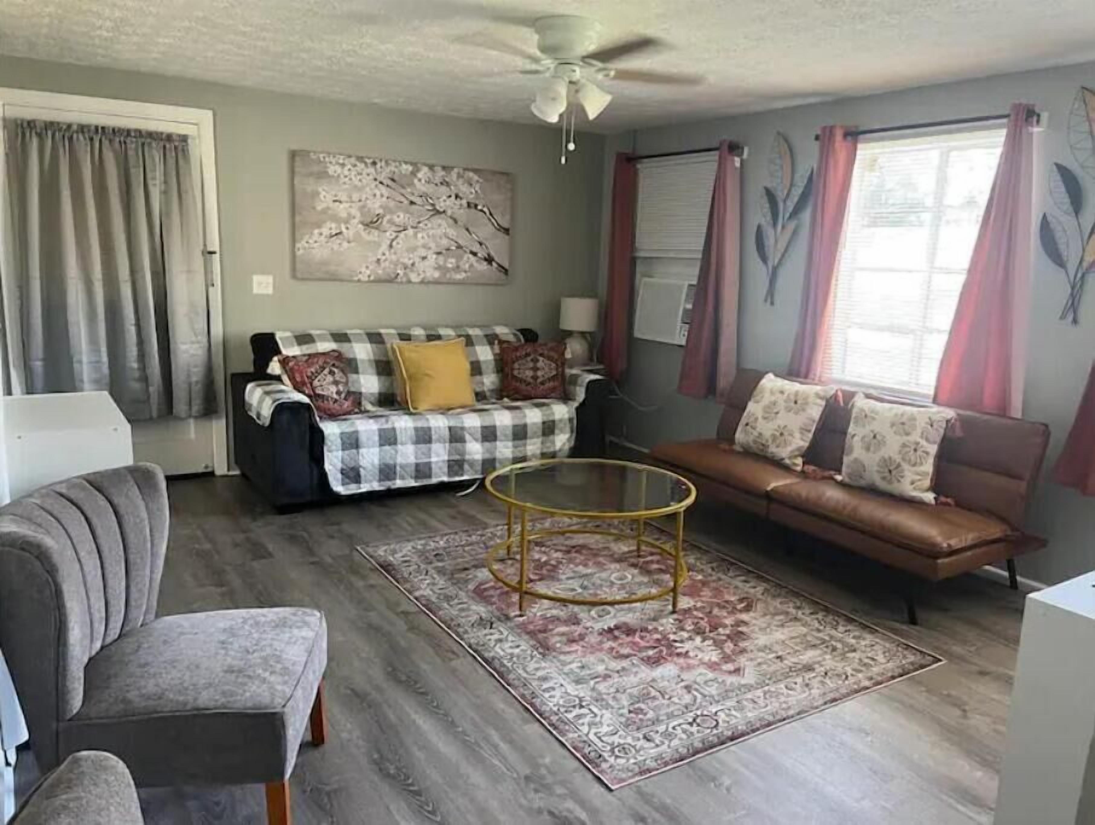 A living room with a checkered sofa, a brown leather sofa, a glass coffee table, and a grey armchair.