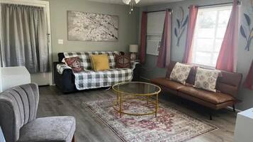 A living room with a checkered sofa, a brown leather sofa, a glass coffee table, and a grey armchair.