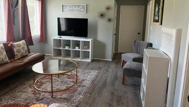 A living room with a sofa, a TV on a white stand, a ceiling fan, and a door in the background. - Historic Peaceful Apt near VSU & SGMC (Valdosta)