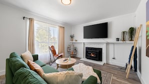 A living room with a green sofa, a fireplace, a flat-screen TV, and a wooden ladder leaning against the wall. - 4-Bedroom Cactus-Themed Retreat with Plush Beds (Sacramento)