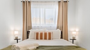 A neatly made bed with a green blanket and white towels, two bedside lamps, and a window with sheer curtains. - 4-Bedroom Cactus-Themed Retreat with Plush Beds (Sacramento)