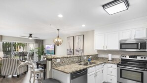 A modern kitchen with white cabinets, a granite countertop, stainless steel appliances, and a dining area with striped furniture. - Maravilla 1201 3/2 pet friendly second floor unit beach service (Miramar Beach)