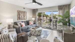 A living room with a grey sofa, striped armchairs, a round ottoman, and a ceiling fan. - Maravilla 1201 3/2 pet friendly second floor unit beach service (Miramar Beach)