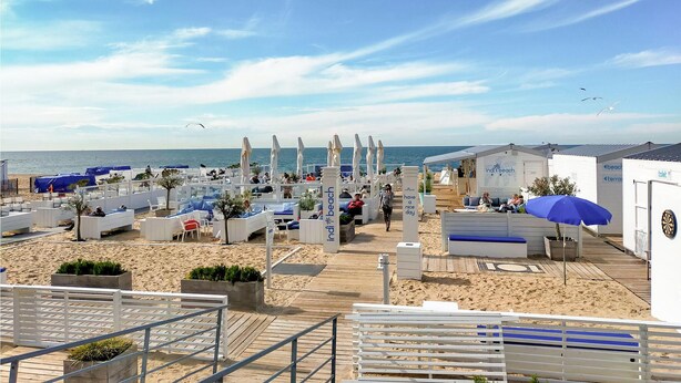 A beachside resort with outdoor seating areas, a boardwalk, and beach umbrellas.