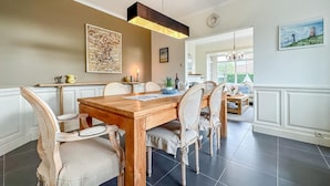 A dining area with a wooden table and wicker chairs, a pendant light, and a painting on the wall.