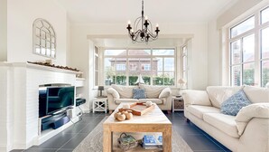 A spacious living room with a fireplace, a large window, and a chandelier.