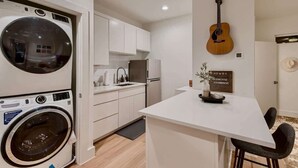 Une petite cuisine équipée d’un lave-linge, d’une guitare et d’une affiche accrochée au mur.