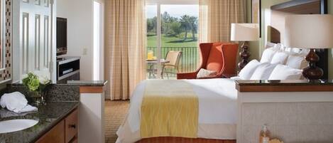 A hotel room with a bed, a desk, a chair, a TV, and a balcony with a view of the outdoors.