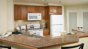 A kitchen with granite countertops, wooden cabinets, a stove, microwave, and refrigerator.