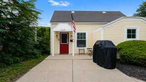 A single-story house with a red door, number 110, a small porch with two chairs, and a covered grill. - Home w/ Garage in DT Libertyville Near Naval Base! (Libertyville)