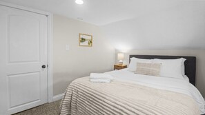 A bedroom with a bed, a nightstand, a lamp, and a door. - Home w/ Garage in DT Libertyville Near Naval Base! (Libertyville)