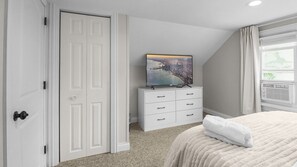 Un dormitorio con cama, cómoda, televisor sobre la cómoda y una puerta.