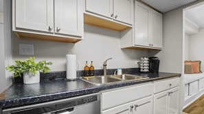 Cocina con armarios blancos, encimera de granito, lavabo, cafetera y planta.