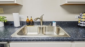 A kitchen with a double stainless steel sink, two soap dispensers, a paper towel holder, and a potted plant. - Home w/ Garage in DT Libertyville Near Naval Base! (Libertyville)