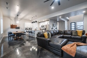 A spacious living area with a black leather sectional sofa, a dining table with chairs, and a kitchen in the background. - Large 5 bedroom with double bunkroom and pool (Hurricane)