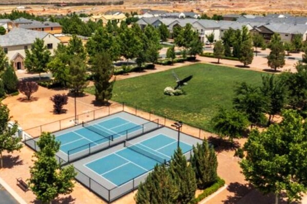 A residential area with two tennis courts, surrounded by trees and houses.
