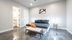Un dormitorio moderno con una cama grande, un banco, una mesita de noche y un ventilador de techo.