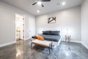Ein modernes Schlafzimmer mit einem großen Bett, einer Bank, einem Nachttisch und einem Deckenventilator.