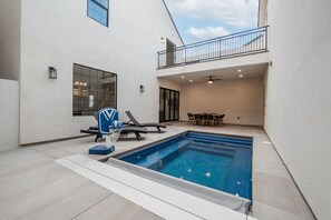 A modern pool area with a sunken hot tub, lounge chairs, and a dining table.