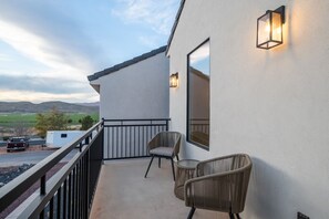 A balcony with two wicker chairs, a white wall, and a view of a trailer and vehicle on a road. - Large 5 bedroom with double bunkroom and pool (Hurricane)