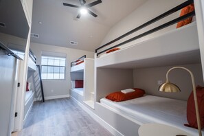 A dormitory room with bunk beds, a ceiling fan, and a window.