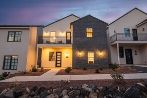 A modern two-story house with a stone facade, a balcony, and a well-lit entrance.