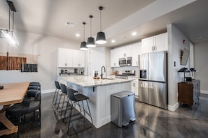A modern kitchen with white cabinets, stainless steel appliances, and a central island with bar stools. - Large 5 bedroom with double bunkroom and pool (Hurricane)