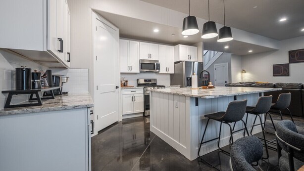 Una cocina moderna con armarios blancos, electrodomésticos de acero inoxidable y una isla central con taburetes de bar.
