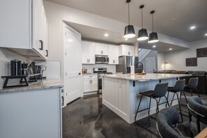 A modern kitchen with white cabinets, stainless steel appliances, and a central island with bar stools. - Large 5 bedroom with double bunkroom and pool (Hurricane)