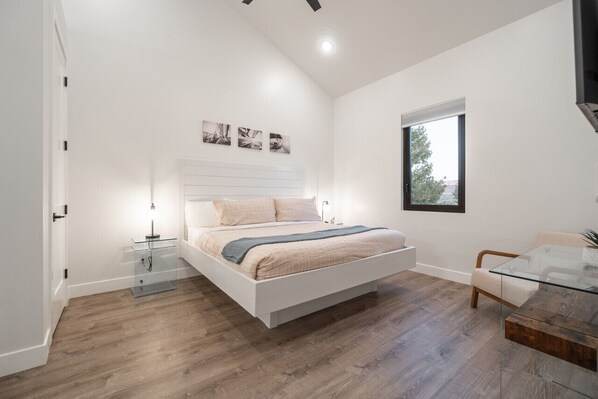 A bedroom with a bed, bedside tables, a glass coffee table, a window, and a view of the outdoors.
