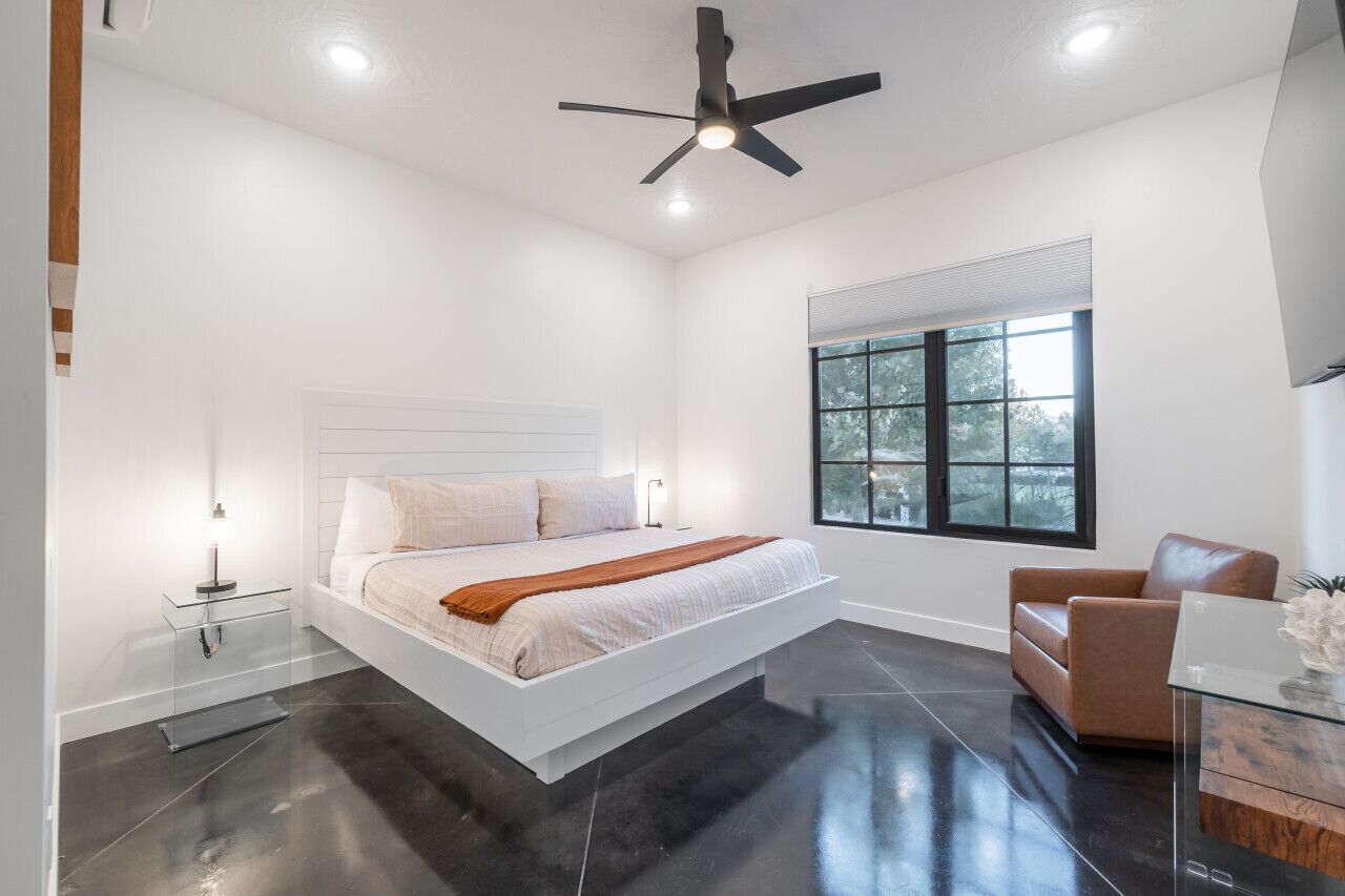 Une chambre moderne avec un lit, un ventilateur de plafond, une fenêtre et une chaise.