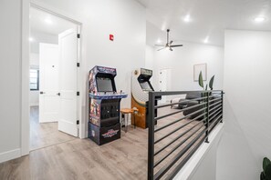 Un intérieur moderne avec un espace dédié aux jeux, comprenant deux bornes d’arcade, un escalier avec une rampe et une décoration minimaliste.